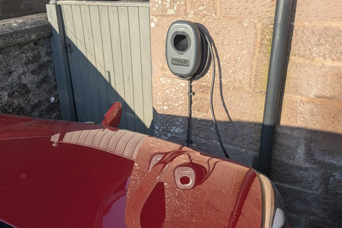 Red electric car charging from wall-mounted EV charger on a stone property in Brechin