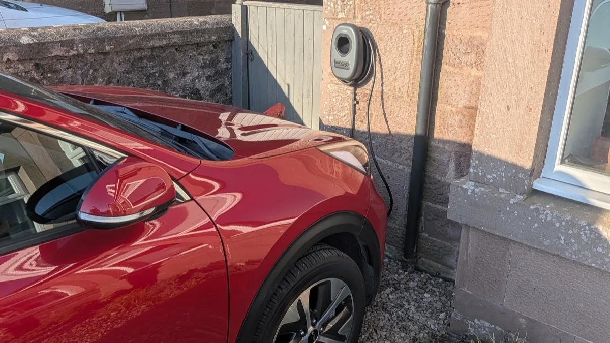 Red electric car charging from a wall-mounted EV charger on a stone property in Brechin, Angus